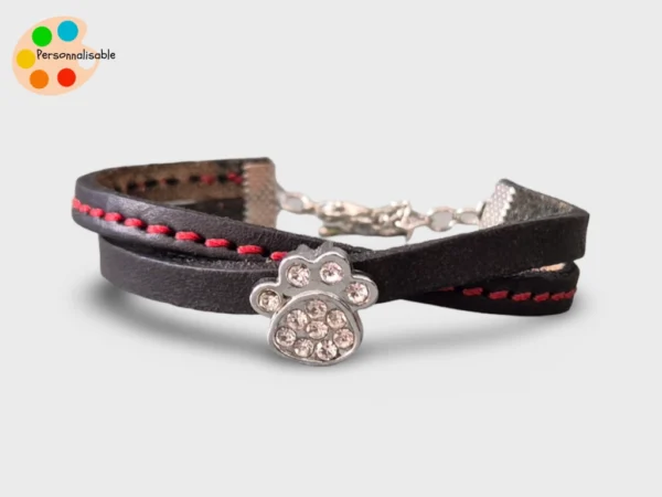 Un bracelet en cuir noir avec une couture rouge et une patte de chien à strass