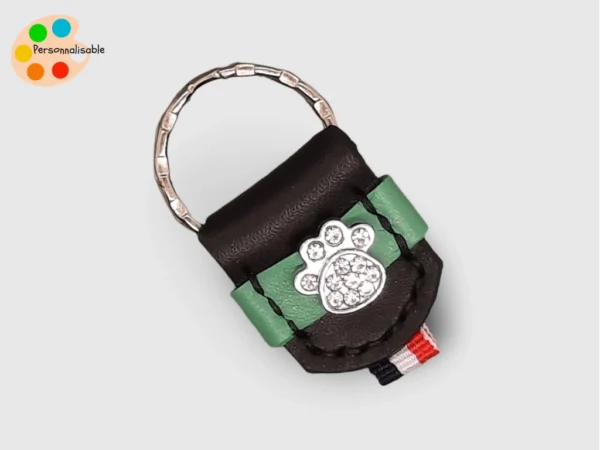 Un porte clé en cuir noir et vert avec une patte de chien à strass